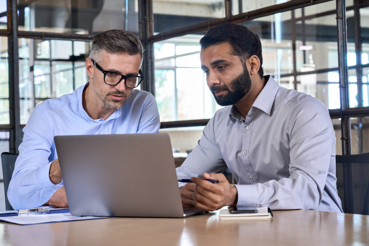 Digitalisierung für lokale Händler: 6 Schritte zum Erfolg Zwei Geschäftsmänner diskutieren konzentriert über digitale Strategien an einem Laptop in einem modernen Büro, symbolisierend die Digitalisierung für lokale Händler.